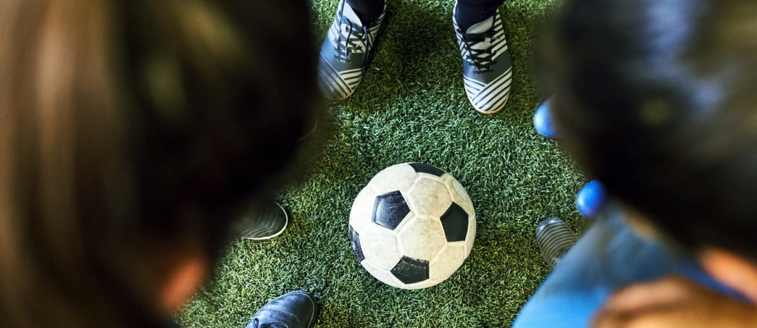 High angle view of a girls team in huddle at sports court with soccer ball in ground. Female players huddling at indoor soccer court.